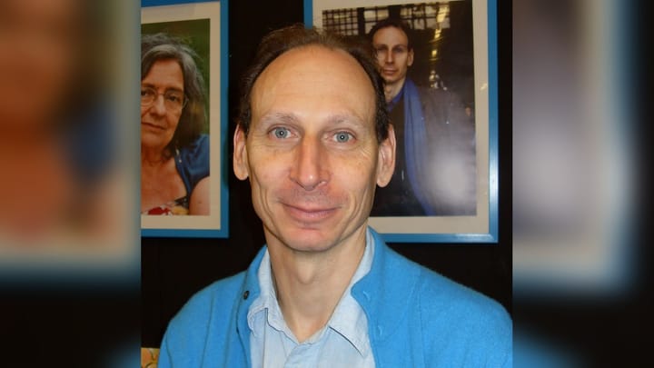 Novelist Richard Zimler in a blue cardigan at the Gothenburg Book Fair in 2008, standing in front of framed author portraits