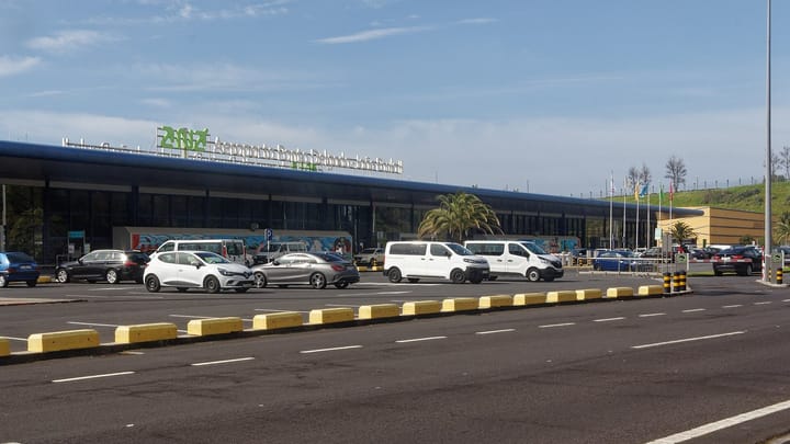The terminal of Ponta Delgada's João Paulo II airport on São Miguel, with its name in green letters on the roof and cars parked in front under a blue sky