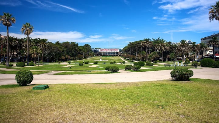 The Casino Estoril seen across the long formal gardens of Estoril, lined with palm trees under a bright blue sky