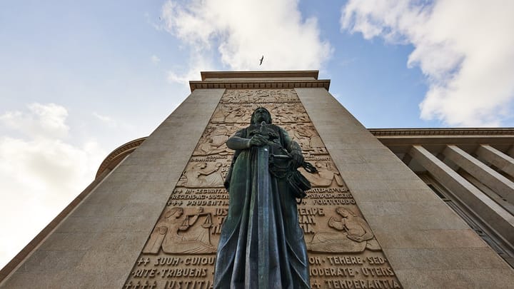 The bronze statue of Justice holding a sword in front of the carved granite tower of the Palácio da Justiça in Porto, seen from below against a cloudy sky