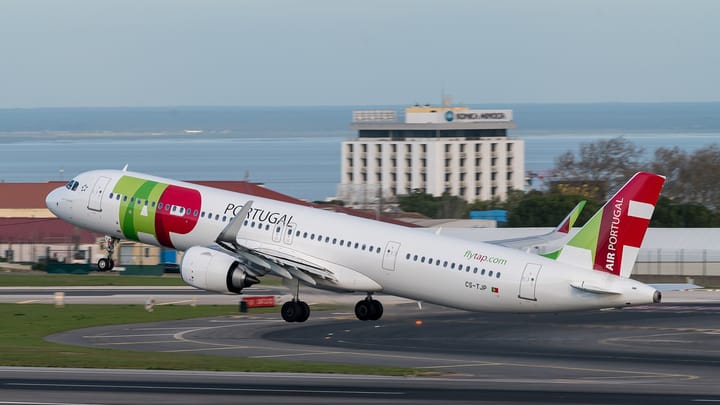 A TAP Air Portugal Airbus A321neo in white and green and red livery lifting off from a runway at Lisbon airport, with the Tagus estuary behind