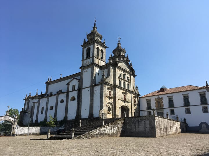 The white and granite baroque front of the Mosteiro de Sao Martinho de Tibaes near Braga, with its twin bell towers and a broad stone stairway rising from a cobbled forecourt
