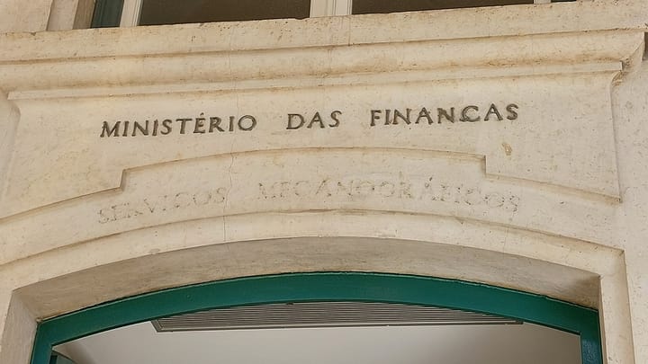 The words Ministerio das Financas carved into the pale stone lintel above an arched green doorway in the east wing of Lisbon's Praca do Comercio