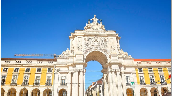 The Rua Augusta Arch on Praca do Comercio in Lisbon, its white stone sculptures and central archway framed by the yellow arcaded buildings of the square