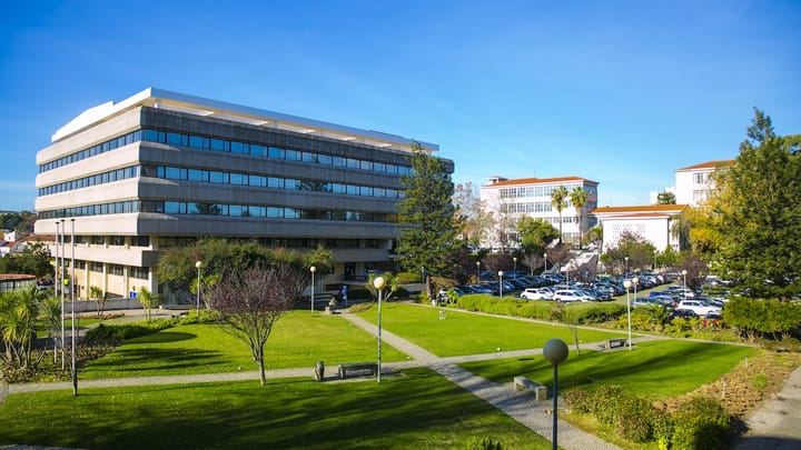 The main building of the Universidade Católica Portuguesa in Lisbon, a six-storey concrete block with ribbon windows behind lawns, paths and trees under a blue sky