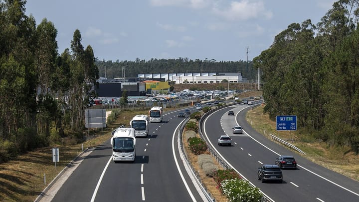 Coaches and cars on the A1 motorway near Fátima, with a sign for Leiria and Porto, eucalyptus on both sides and a lorry depot and warehouses beyond