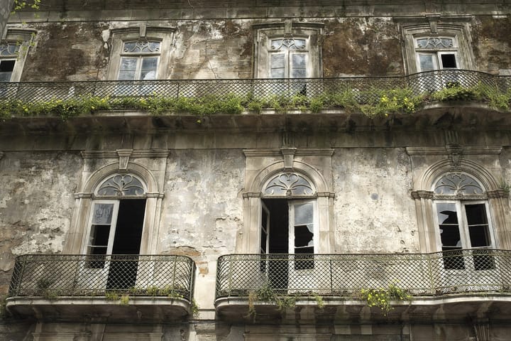 The decayed stone facade and ironwork balconies of the abandoned Caldas de Moledo hotel in the Douro valley, with plants growing from the balcony ledges.