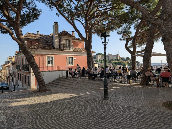 A busy restaurant terrace at the Miradouro da Graca in Lisbon, with Sao Jorge castle on the hill behind