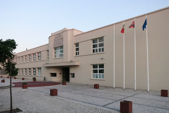 The pale facade and flagpoles of Escola Secundaria Diogo de Gouveia in Beja, with the original Liceu Nacional lettering above the entrance