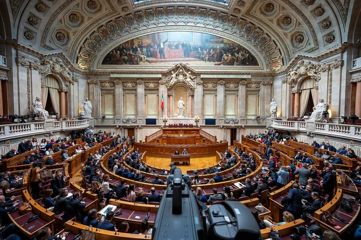 The plenary chamber of the Assembleia da Republica in Lisbon seen from above during a full sitting, with members at their curved wooden benches beneath the painted vault