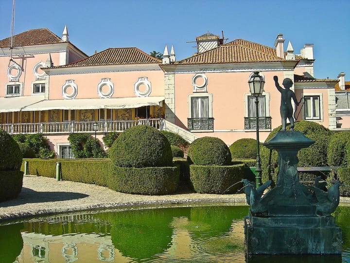 The pink Palacio de Belem in Lisbon, the official residence of the President of the Republic, seen from its formal garden across a fountain and clipped box hedges