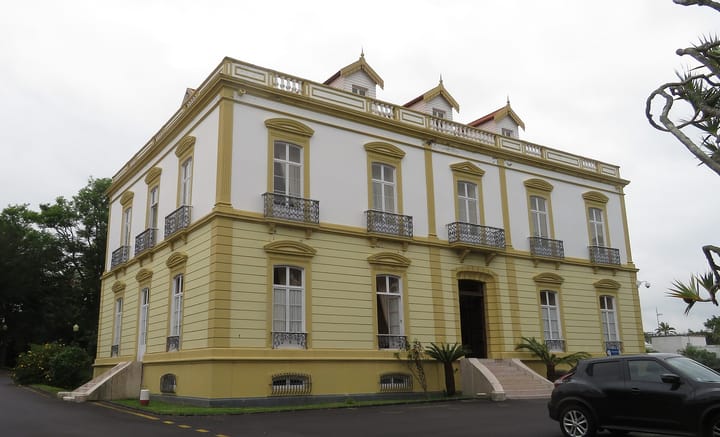 The rectory of the Universidade dos Acores in Ponta Delgada, a two-storey yellow and white building with wrought iron balconies and three dormer windows on the roof