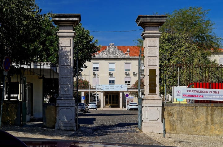 The stone gateposts and main entrance of the Hospital Dona Estefânia in Lisbon, with a nurses' union banner reading Fortalecer o SNS hung on the boundary wall