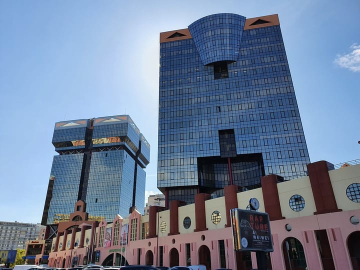 The two blue glass Amoreiras towers rising above their pink and cream shopping centre in Lisbon against a clear sky