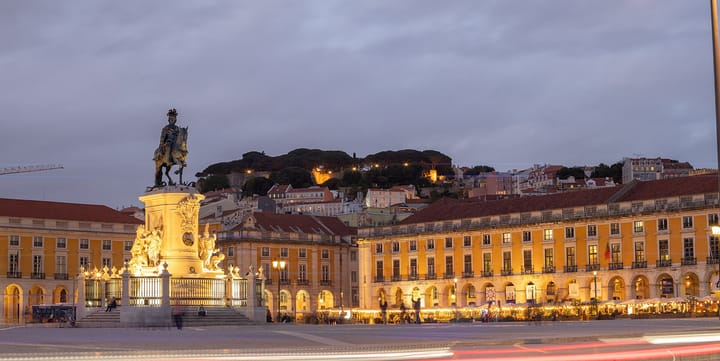 Lisbon's Praça do Comércio at dusk, the lit equestrian statue of King José I in the foreground and the yellow arcaded buildings and Castelo de São Jorge beyond