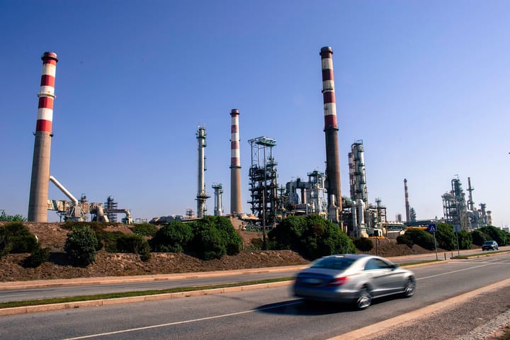 Red and white chimneys and processing towers of the former Galp oil refinery at Leça da Palmeira in Matosinhos, with a car passing on the road in front