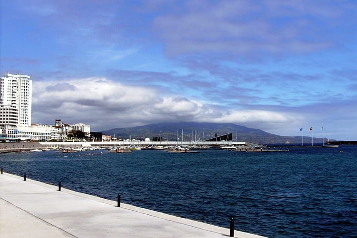 The Portas do Mar waterfront and marina in Ponta Delgada, with sailing boats, a white tower block and green hills under cloud