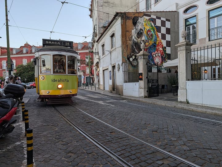 A green and yellow Lisbon tram on route 28 to Graça climbing a cobbled street past old houses and a large painted mural