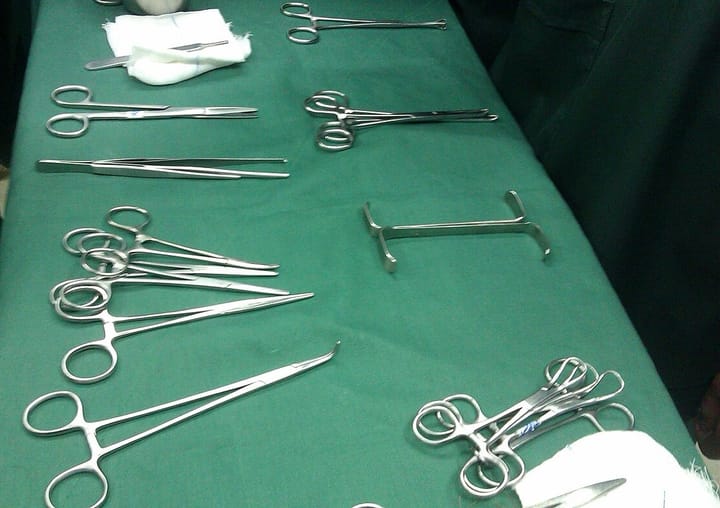 Surgical instruments, forceps, scissors and a retractor, laid out on a green sterile cloth before an operation