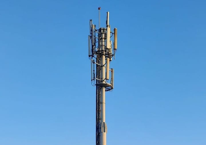 The top of a shared mobile phone mast carrying several antenna panels against a clear blue sky