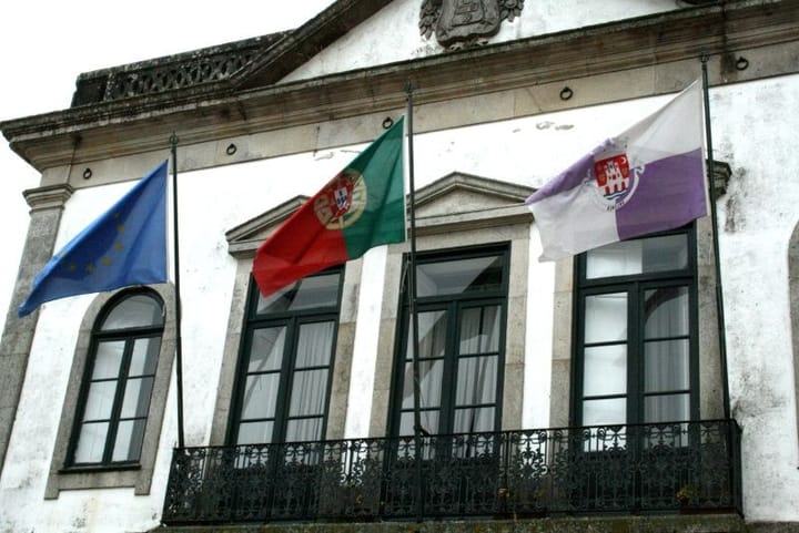 The European Union flag, the Portuguese flag and a municipal flag flying from the balcony of a white town hall in Portugal