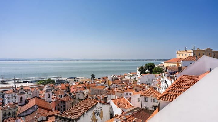 The red-tiled rooftops of Alfama running down to the wide blue Tagus estuary in Lisbon on a clear day