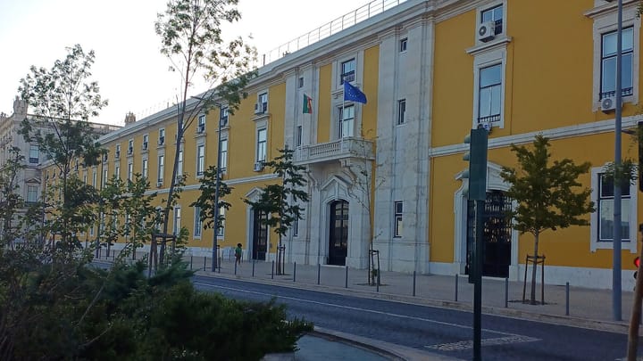 The long yellow facade of the Finance Ministry building on Lisbon's waterfront, with the Portuguese and EU flags over the balcony
