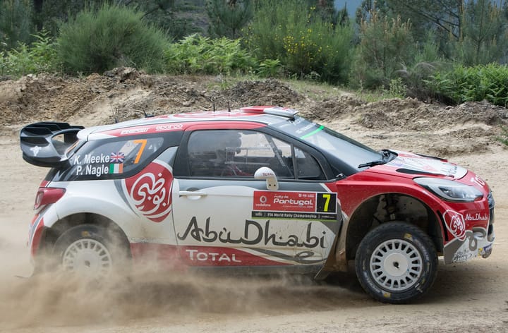 A red and white Citroën World Rally Car kicks up dust on a gravel stage of the Rally de Portugal in the Marão hills in 2016