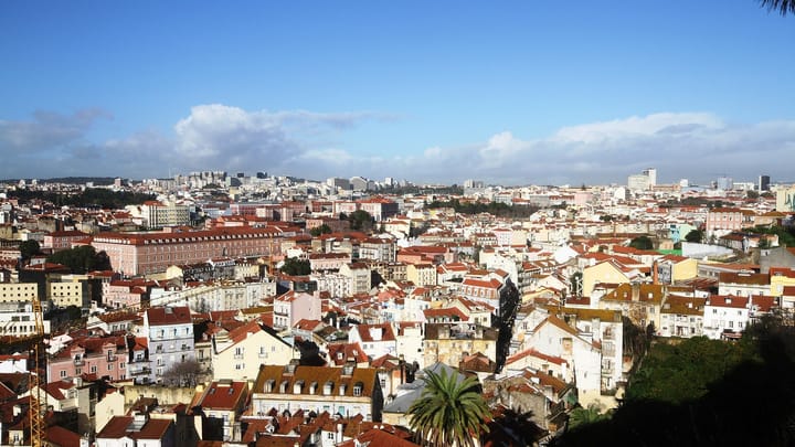 Lisbon's red rooftops seen from the Graça viewpoint, looking across the city centre toward the São José hospital district under a blue sky