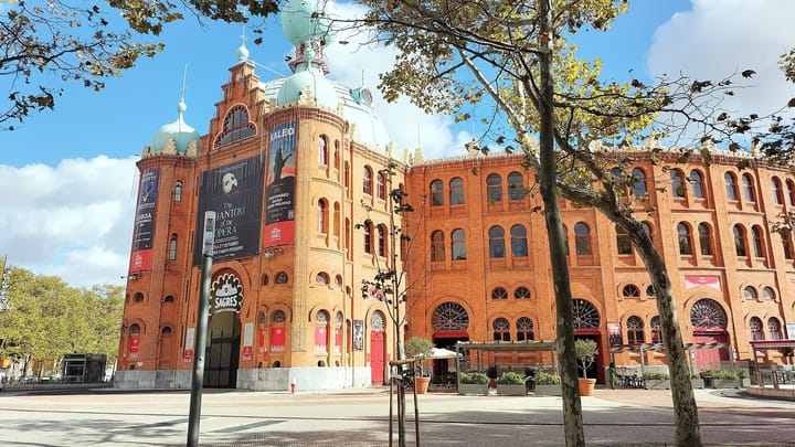 The red-brick Campo Pequeno bullring in Lisbon, with its Moorish-style towers and green onion domes, seen through plane trees under a blue sky