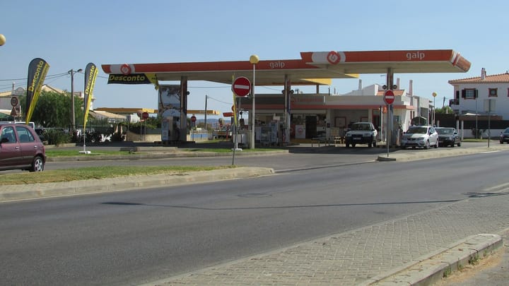 A Galp filling station forecourt with orange and white canopies and parked cars beside a road in Vale da Azinheira, Albufeira, under a clear sky