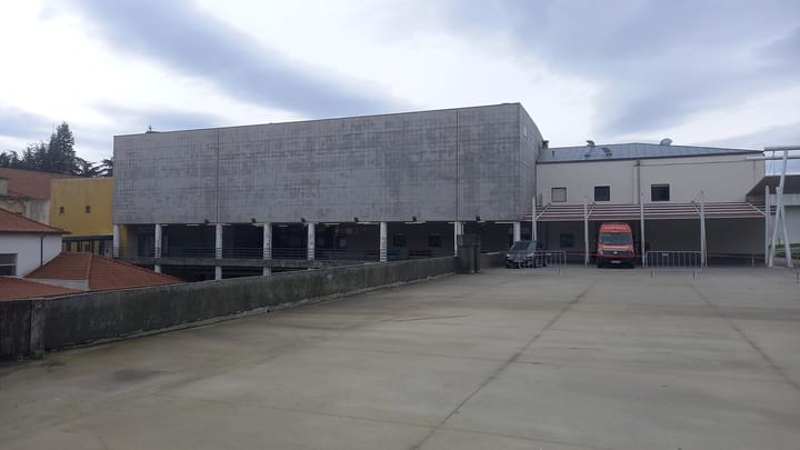 The emergency department entrance of the hospital in Guarda, a grey concrete block with a red ambulance parked under a covered bay, seen across an empty car park
