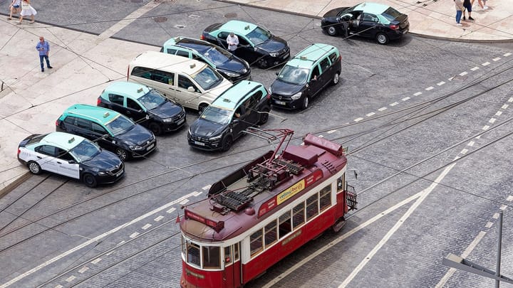 A red tourist tram passes taxis waiting beside Praça do Comércio in Lisbon, seen from above