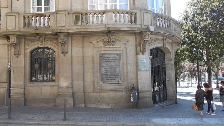 The granite corner entrance of the Montepio building on Avenida dos Aliados in Porto, with a Montepio sign and an engraved plaque beside wrought-iron doors